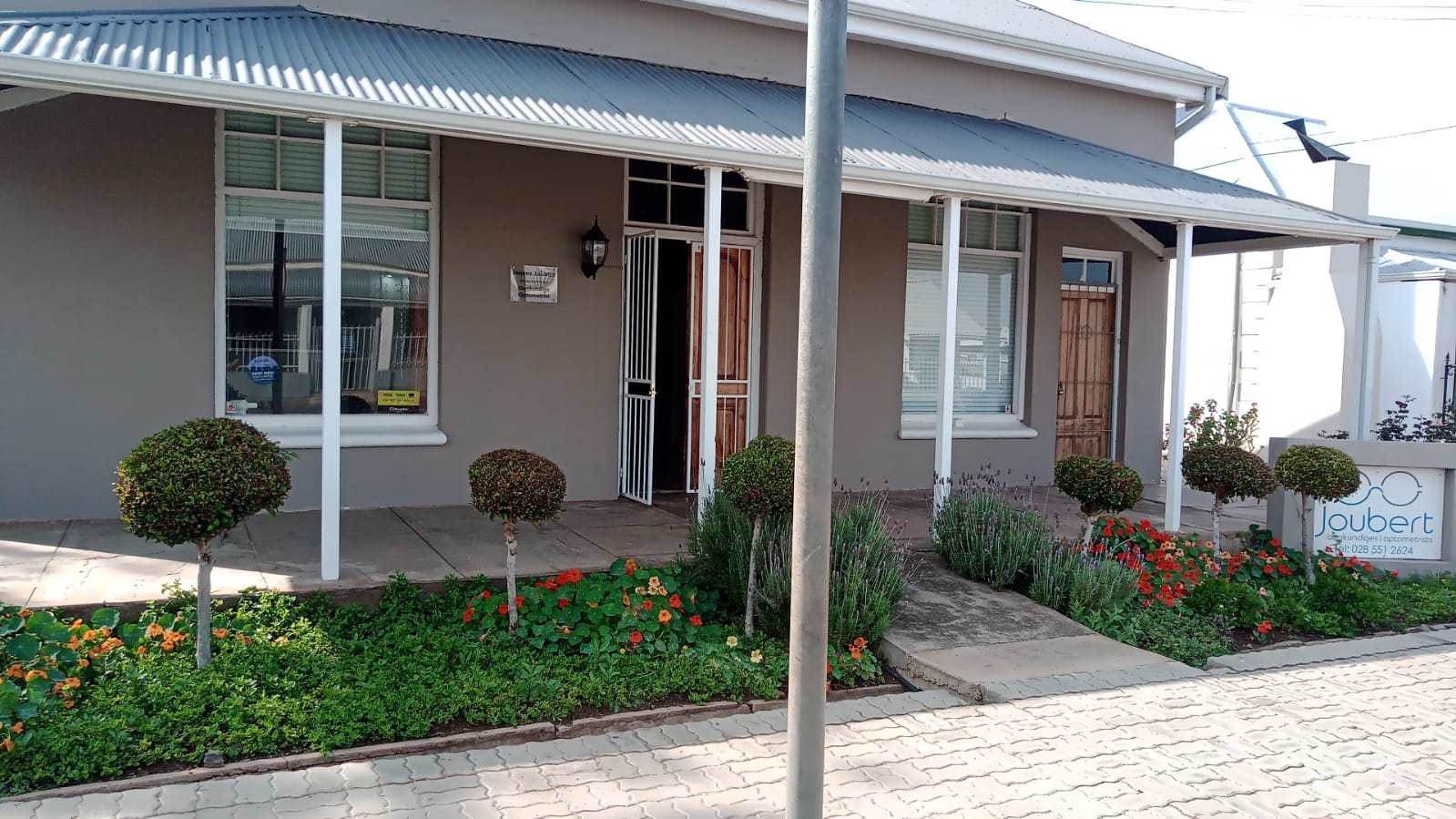 Joubert Oogkundiges branch exterior with eyewear sign, porch pillars and garden in bloom